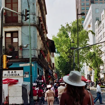 Busy urban street scene with people walking, tall buildings, trees, and a sign for Bar Florida.