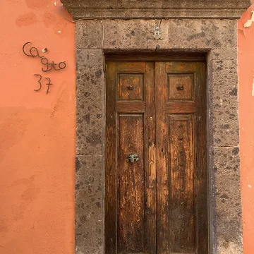 Weathered wooden door with stone frame set in an orange wall, with black wrought iron house number 37 to the left.