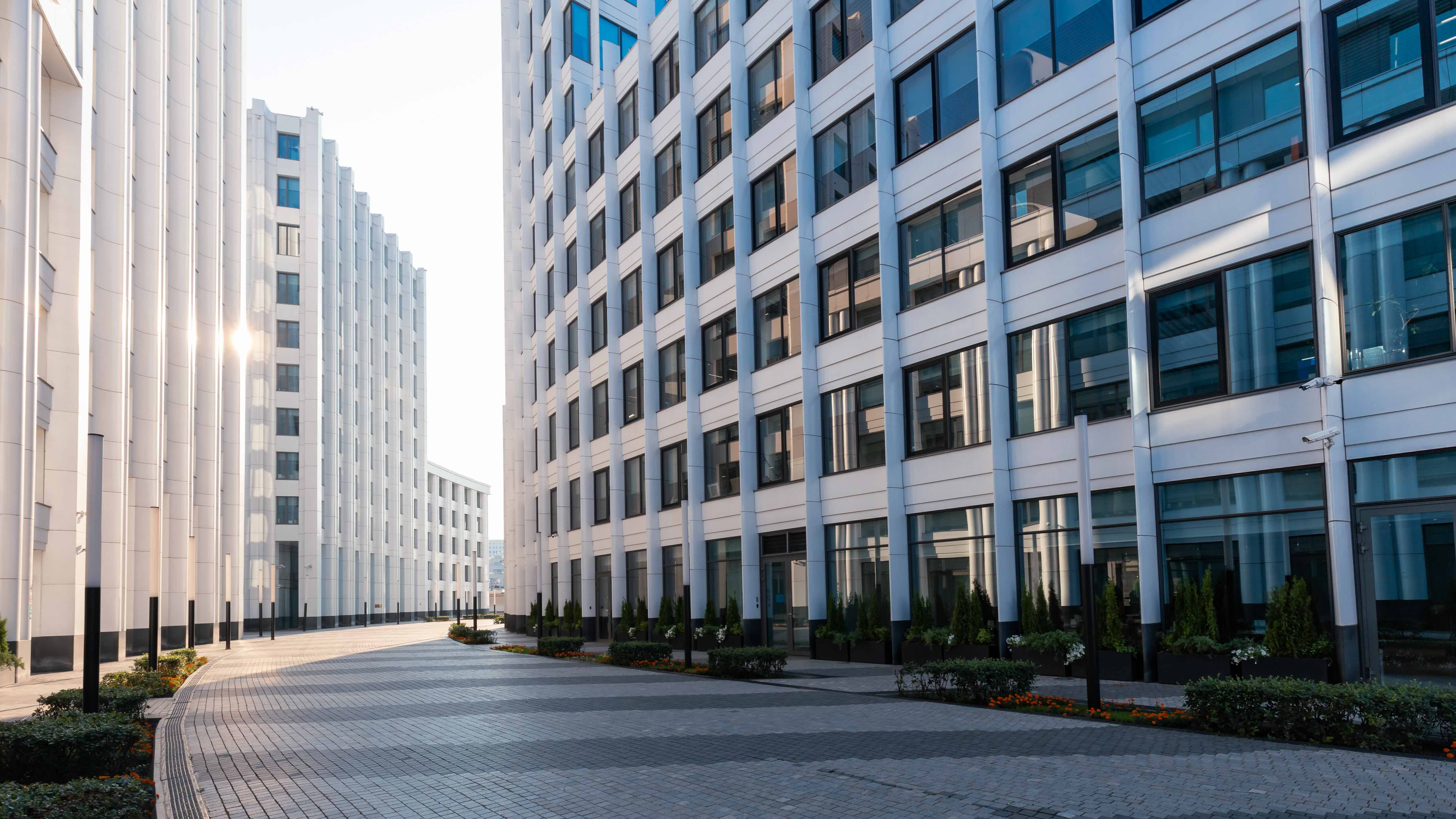 Heller gepflasterter Weg zwischen modernen Bürogebäuden mit reflektierenden Fenstern.