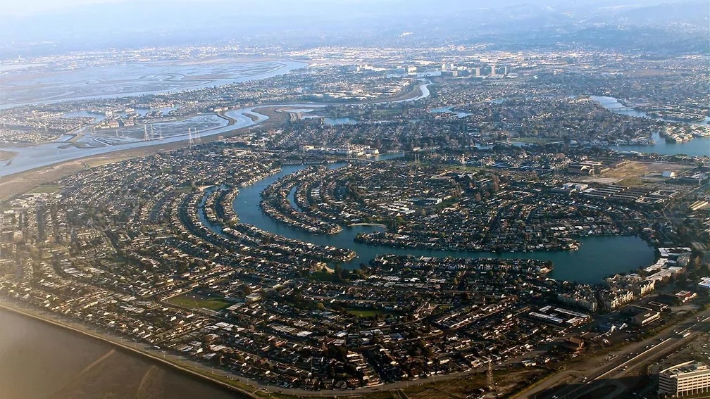 Luftaufnahme einer Wohnsiedlung mit kreisförmigen Wasserwegen und dicht angeordneten Häusern in einem Vorort.