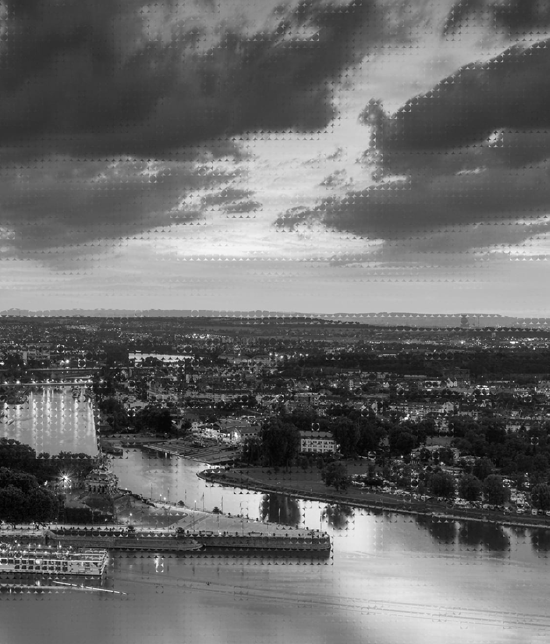 Wide aerial view of a city along a river under a cloudy sky at dusk.