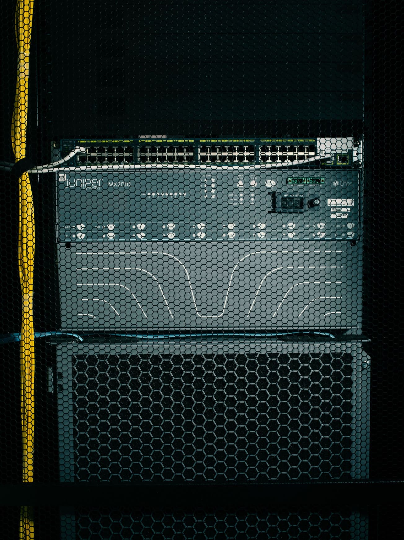 Network server equipment with multiple Ethernet ports behind a black hexagonal mesh panel and yellow cables on the left.