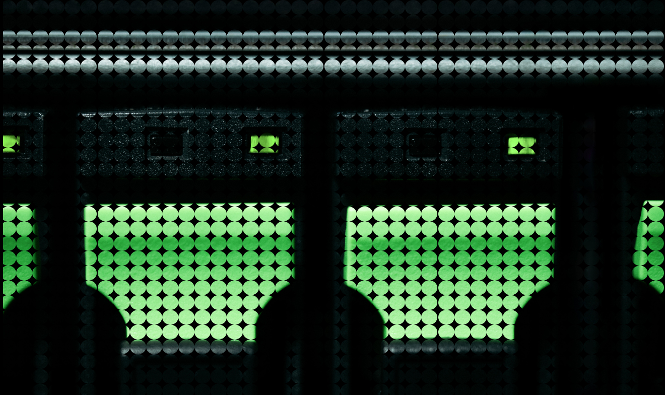 View through a mesh screen of a green grassy field and a window divided by dark vertical bars.
