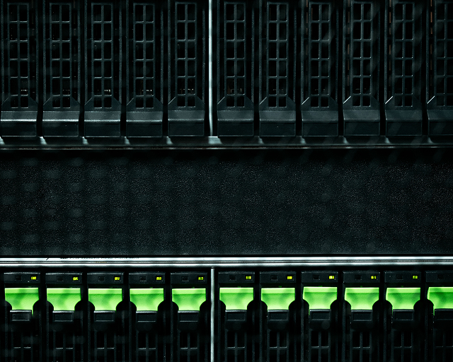 Close-up of black server hardware with glowing green indicator lights in a dark data center rack.