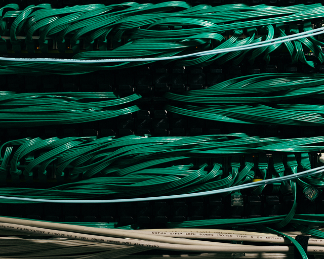 Close-up of organized green network cables connected to a patch panel with white Ethernet cables labeled CAT.6A at the bottom.
