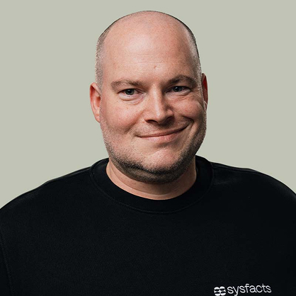 Portrait of a man with light beard wearing a brown blazer and black turtleneck, with sunlight casting shadows on his face.