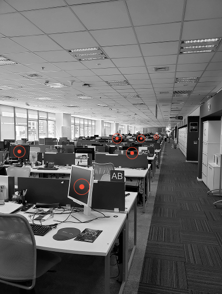 Großraumbüro mit mehreren Reihen von Schreibtischen und Computern, wenige Menschen sind im Hintergrund zu sehen.