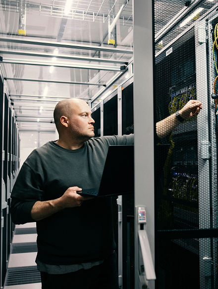 Ein Mann mit Laptop überprüft Serverhardware in einem modernen Rechenzentrum.