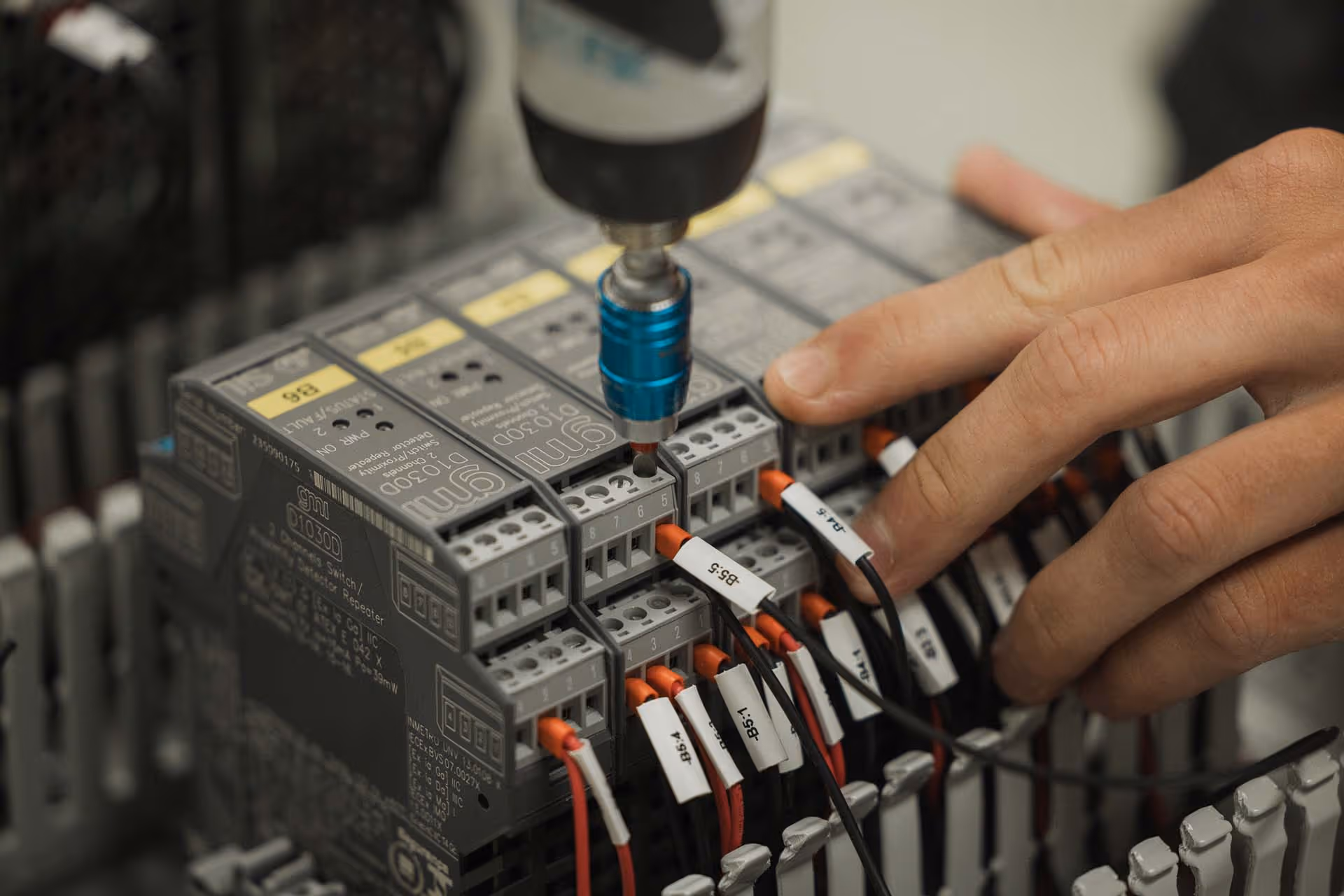En hånd bruker en skrutrekker til å feste ledninger i en elektrisk koblingsboks.