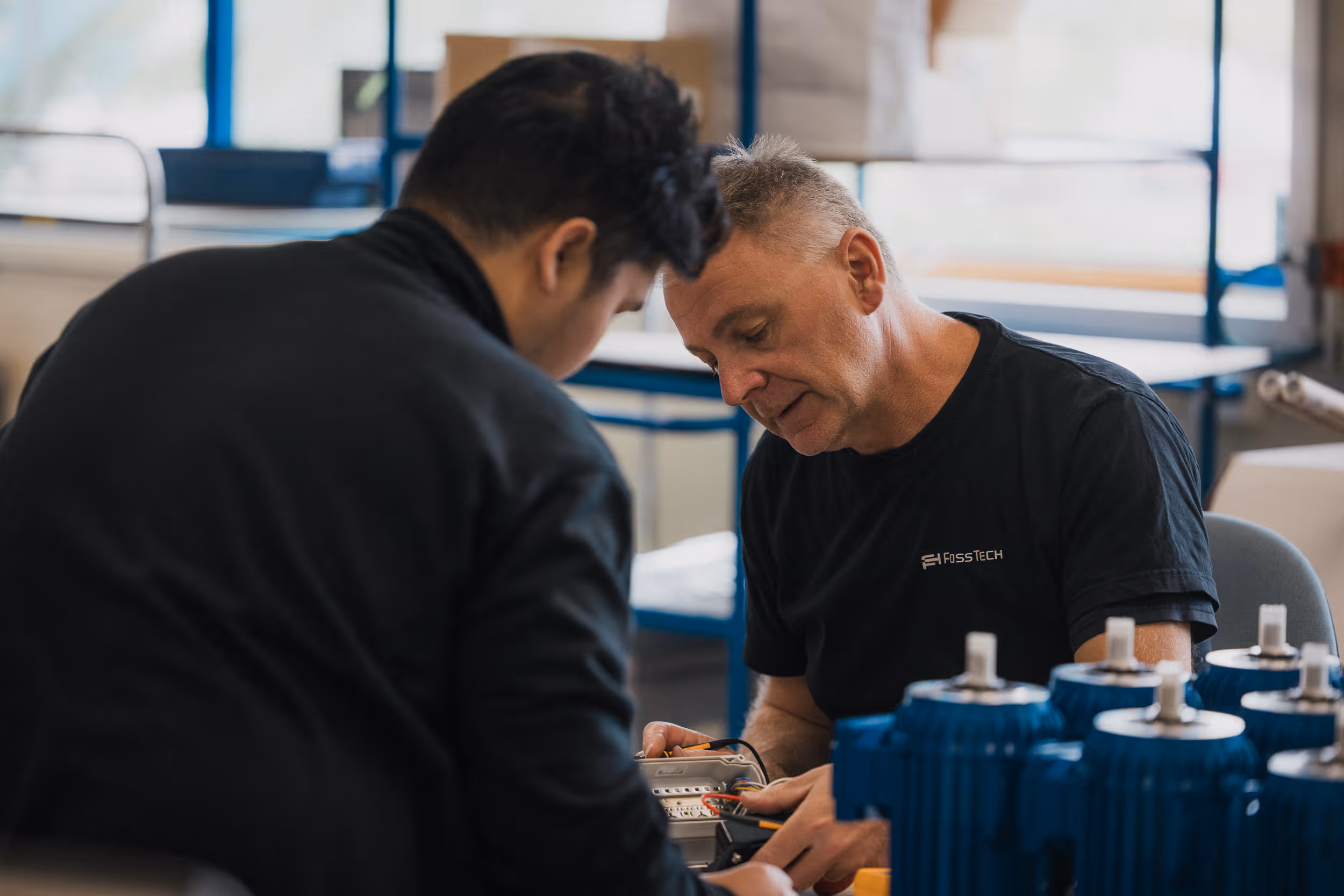 To menn som samarbeider om å inspisere og reparere elektrisk utstyr på et verksted.