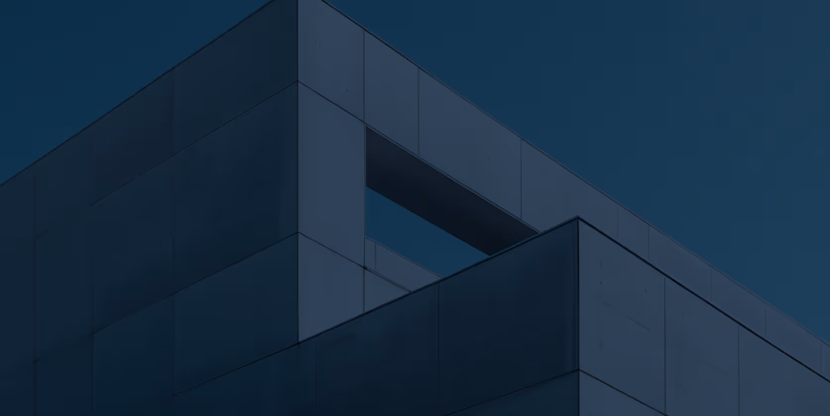 Detail moderního budovy s čistými liniemi a velkými panelovými stěnami za soumraku.