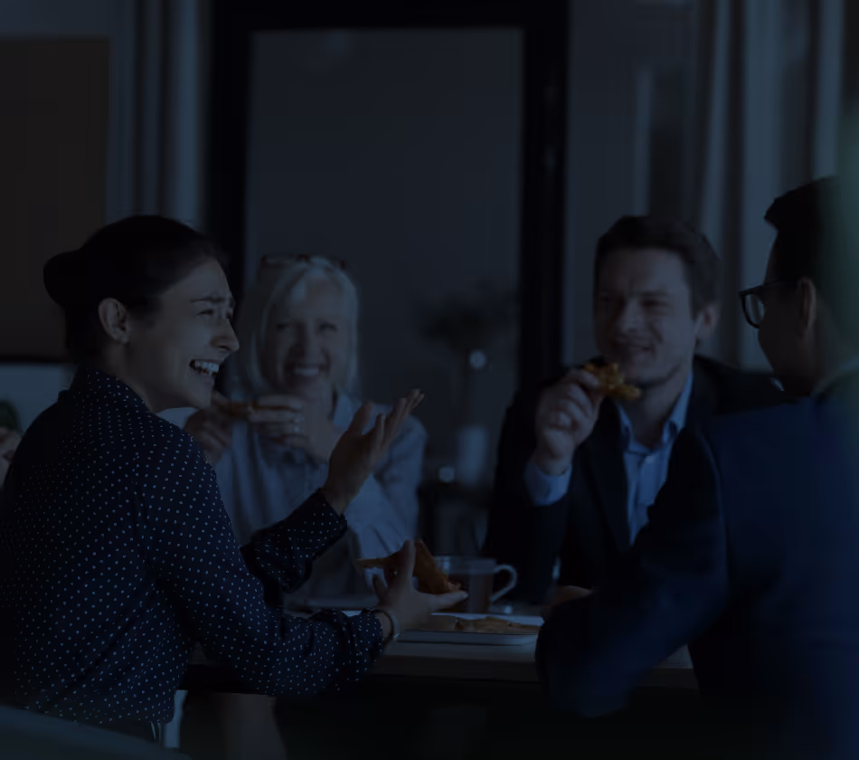 Skupina čtyř lidí sedící u stolu, smějící se a konzumující jídlo během přátelského setkání.