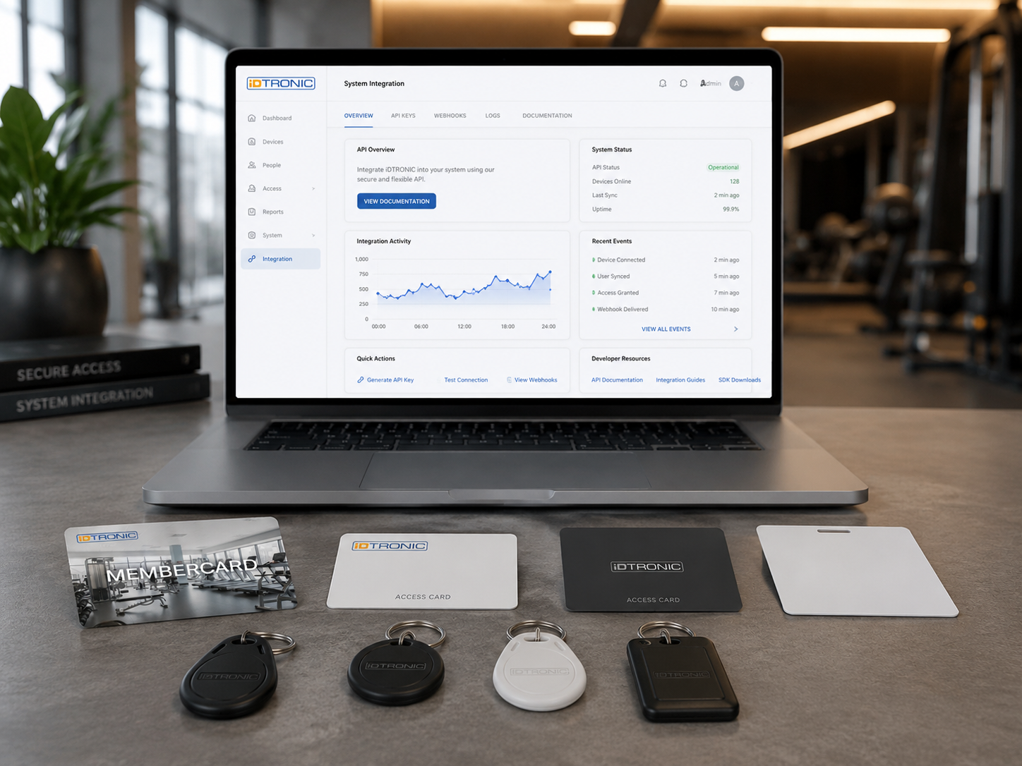 Laptop on desk showing IDTRONIC system integration dashboard with access cards and key fobs below.