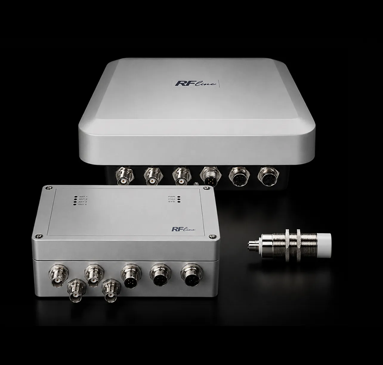 Zwei graue RF-Line Geräte mit mehreren Anschlussbuchsen und ein einzelner metallischer Stecker.