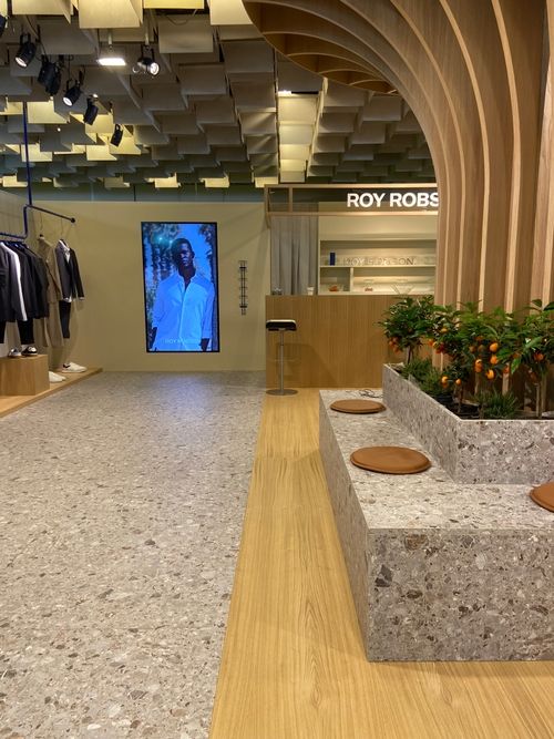 Allestimento Roy Robson a Pitti Uomo 2024, focus sull’isola centrale con agrumi e sedute, pavimento effetto pietra, maxi schermo e bancone hospitality.
