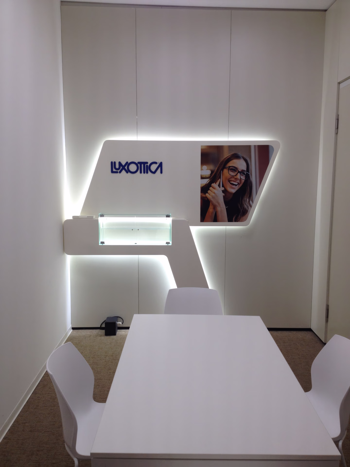 Parete con logo Luxottica, pannello retroilluminato con foto di donna con occhiali, in una sala riunioni.