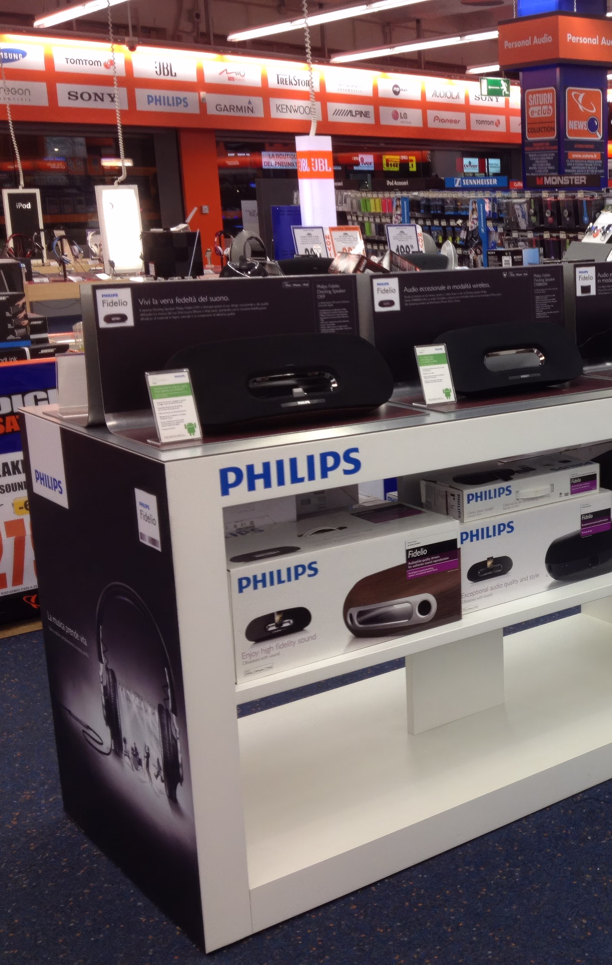 Isola espositiva Philips in un grande negozio di elettronica, con soundbar e altoparlanti in prova e confezioni prodotto a vista.