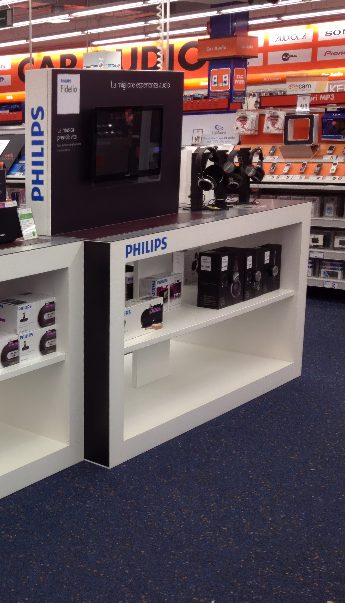 Espositore Philips per la GDO, con testata illuminata e schermi, scaffali con confezioni e prodotti in prova in un punto vendita di elettronica.