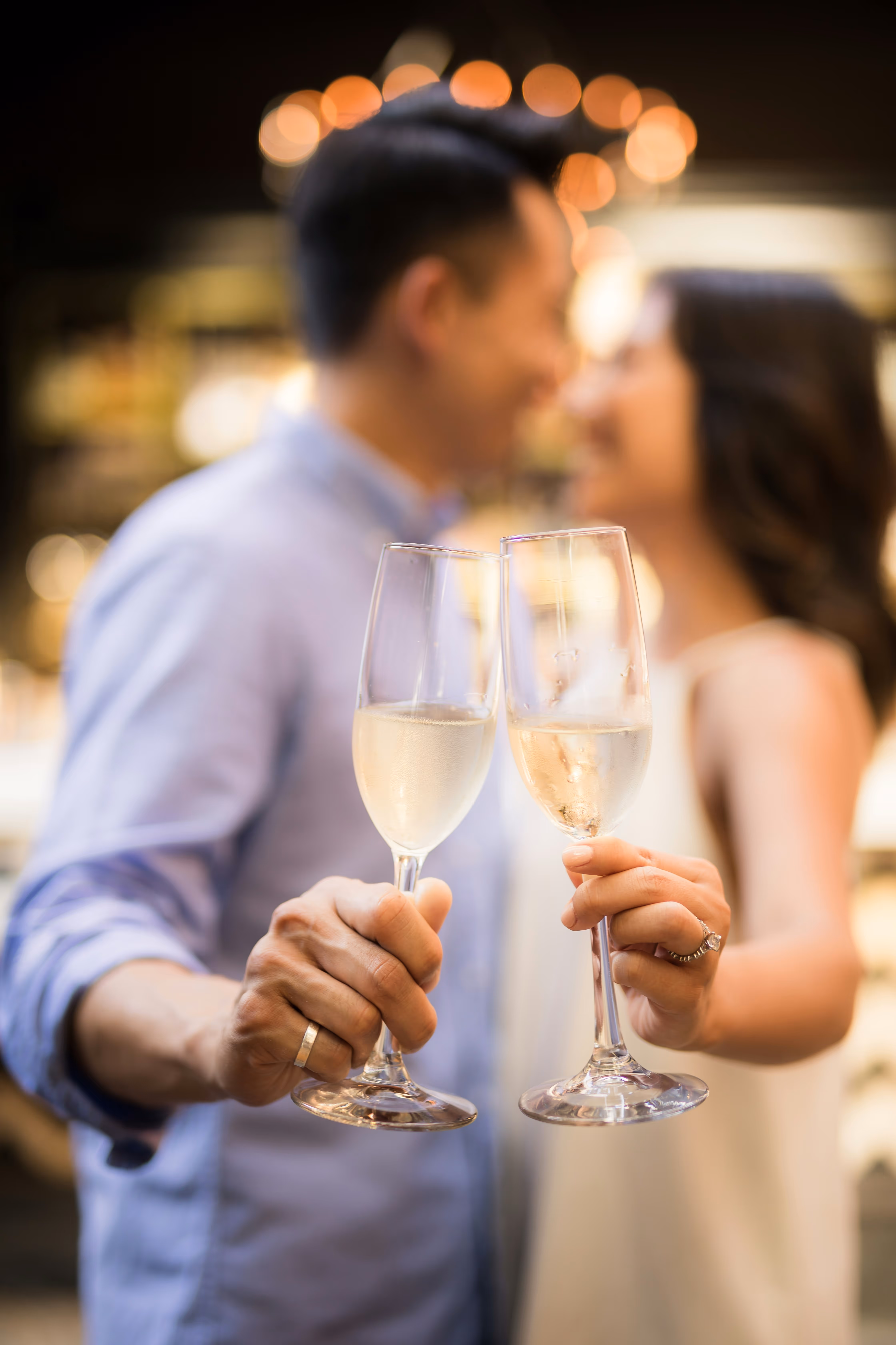 Couple holding and toasting two champagne glasses, with their blurred faces close together in the background.