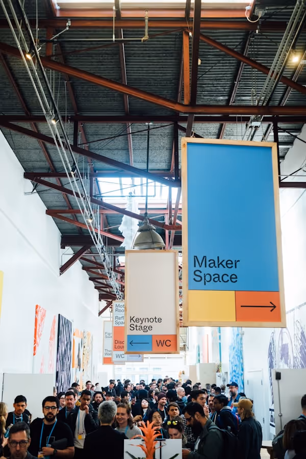 Crowded indoor event with hanging signs indicating directions to Maker Space and Keynote Stage.