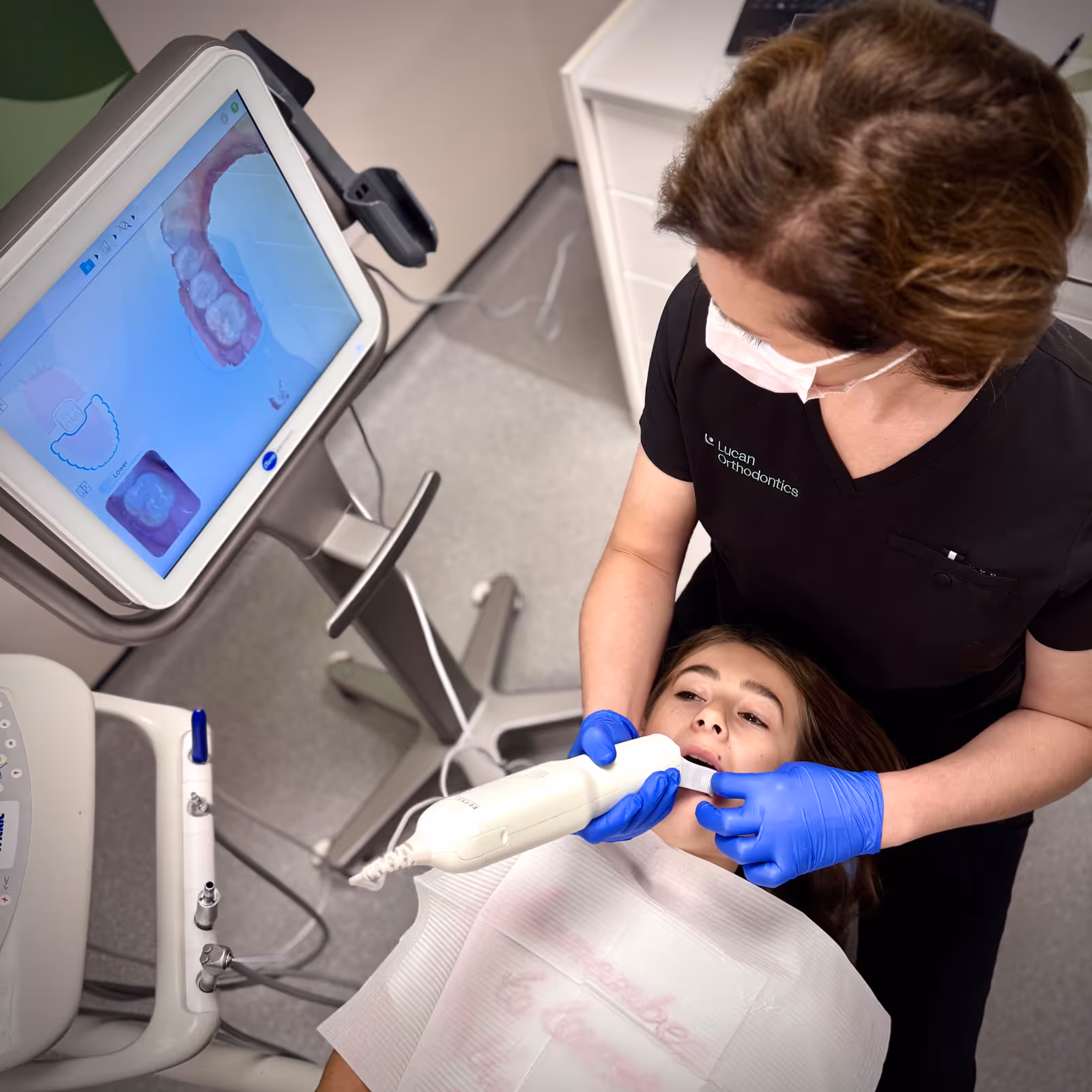 Dentist pointing at a dental X-ray on a screen while discussing it with a patient seated in a dental chair.