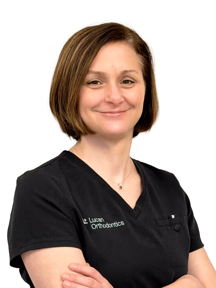 Smiling woman in dark gray medical scrubs with arms crossed.