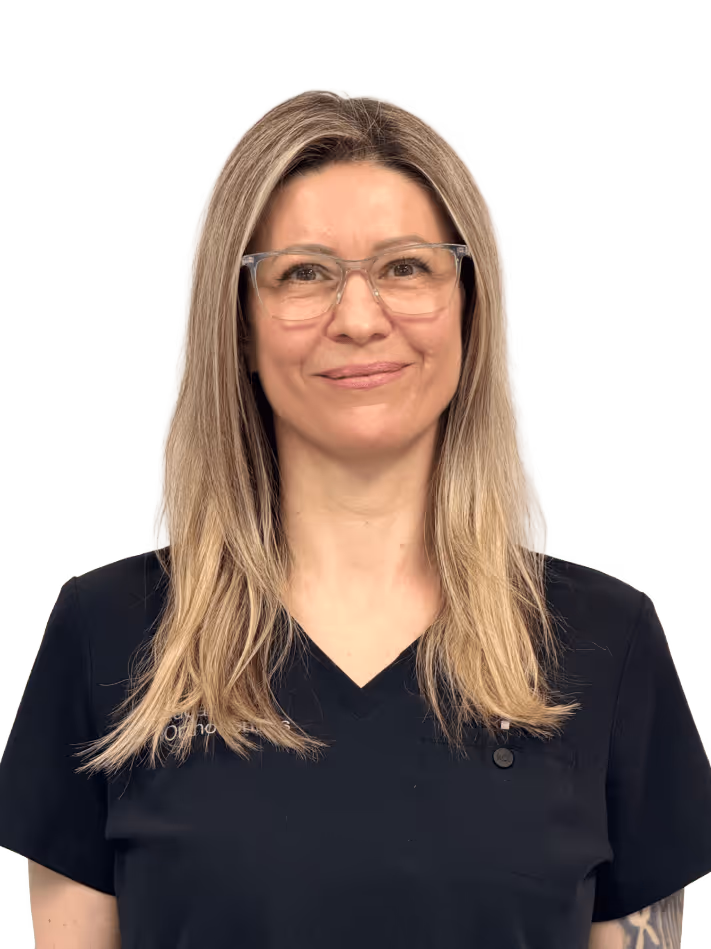 Smiling healthcare professional in grey scrubs with arms crossed.