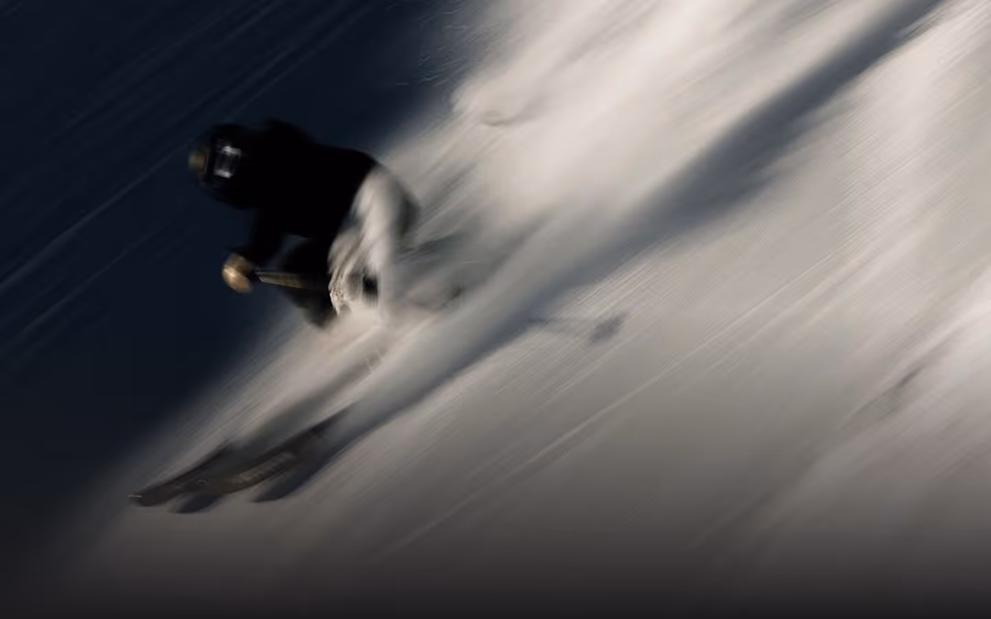 Skier in black jacket and white pants skiing fast down a snowy slope, creating a trail of snow dust.