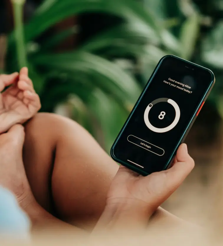 Person holding a phone displaying a mood tracking app with a score of 8 and the text 'Good evening Alice, How’s your mood today?'