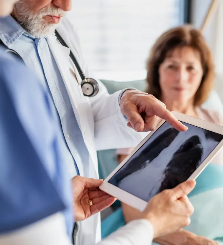 Two doctors reviewing a lung X-ray on a tablet while a female patient looks on in a medical setting.