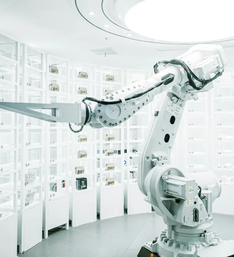 White robotic arm with a flat gripper in a high-tech, white laboratory with multiple small compartments.