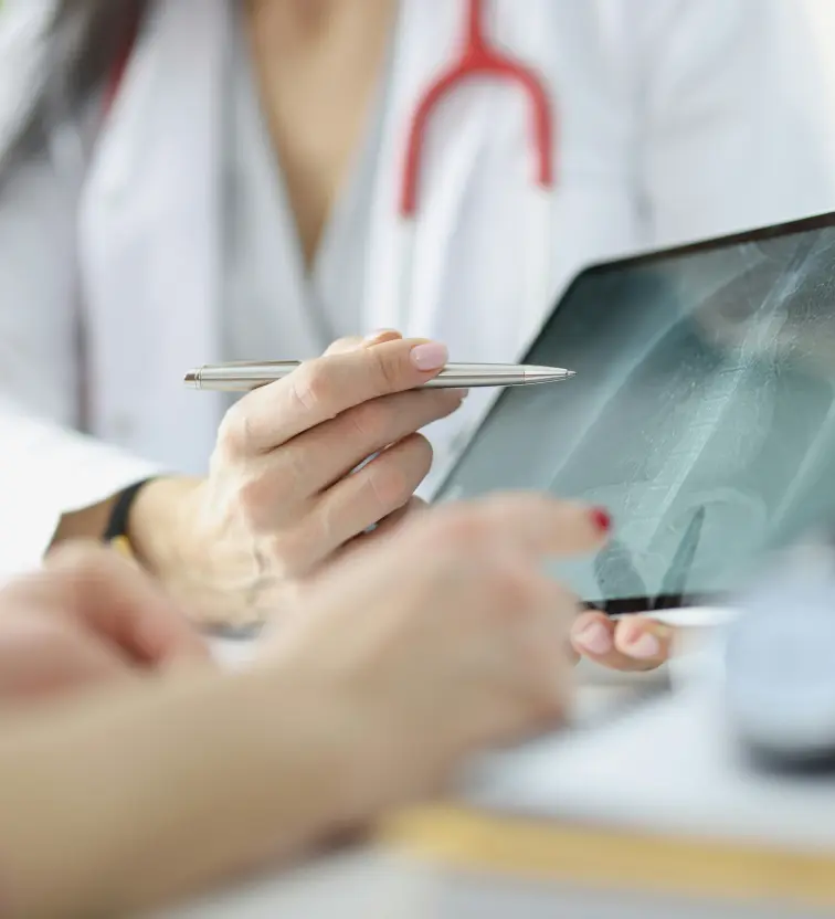 Doctor pointing at a chest X-ray on a tablet while discussing it with a patient.