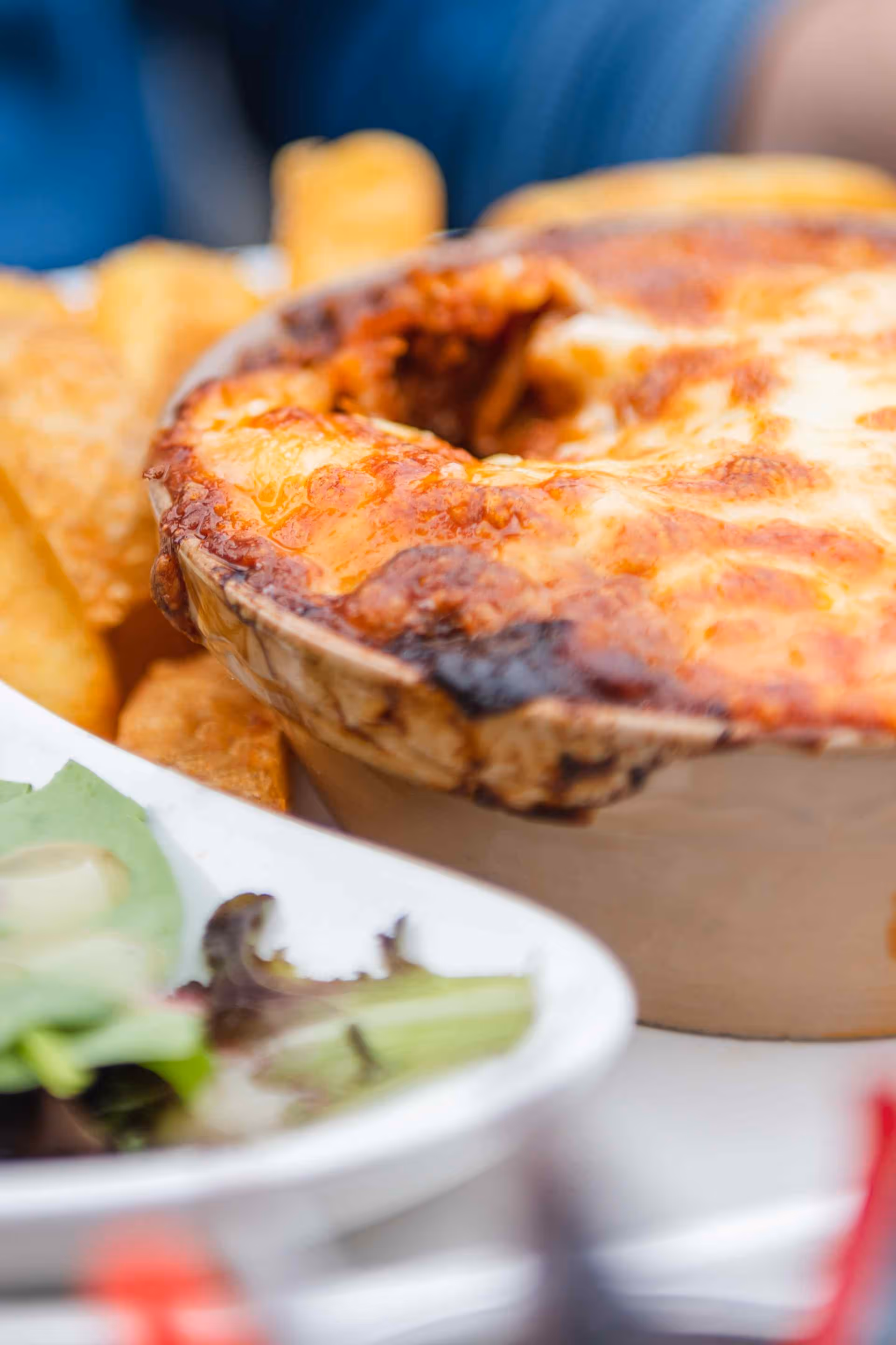 Close-up of a baked dish with melted cheese, served with thick-cut fries and a side salad.