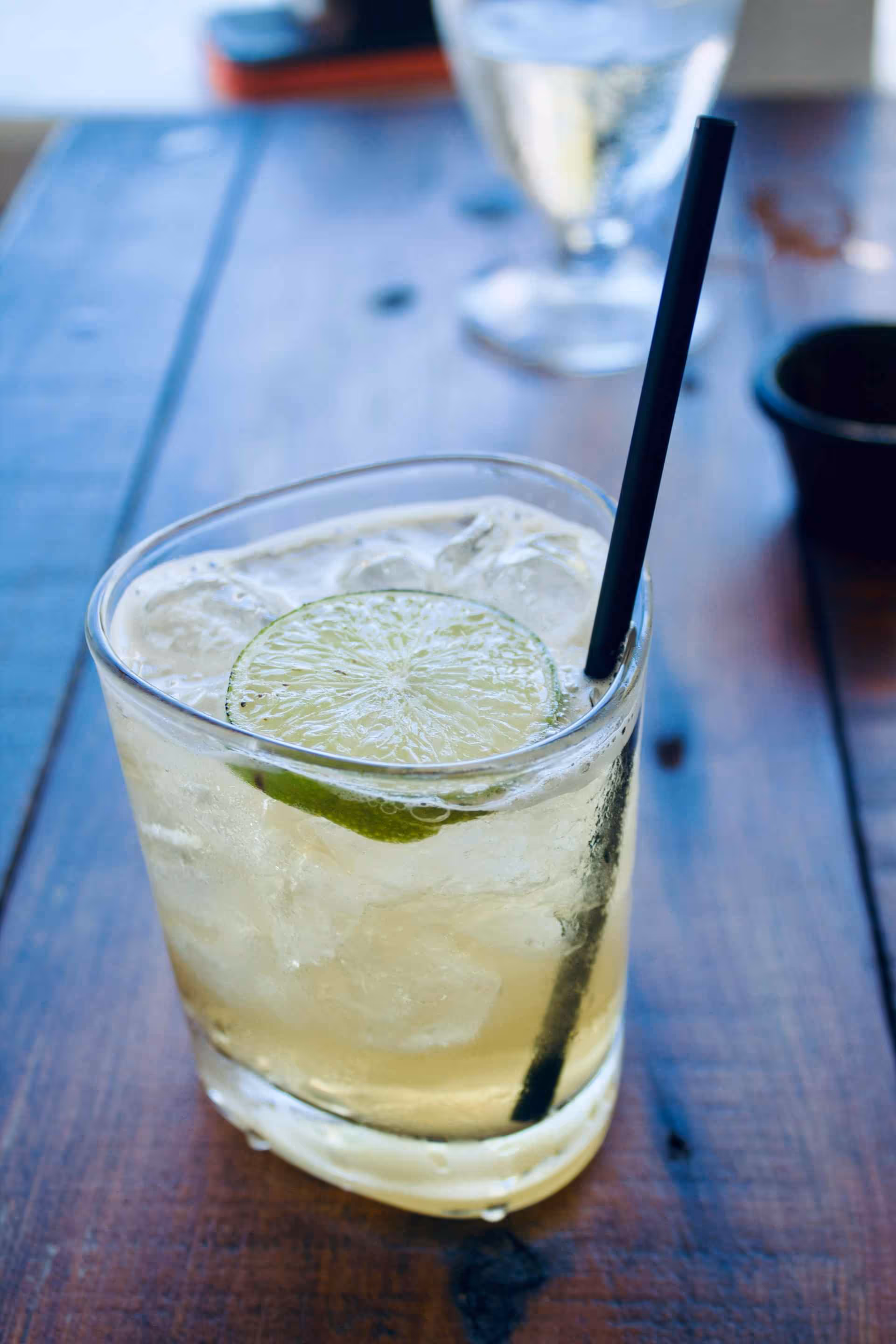 Glass of iced drink garnished with a lime slice and a black straw on a wooden table.