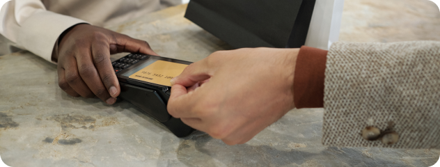 Two people making a payment using a credit card and a card reader on a marble surface.