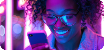 Smiling woman with glasses looking at her smartphone under purple and blue neon lights.
