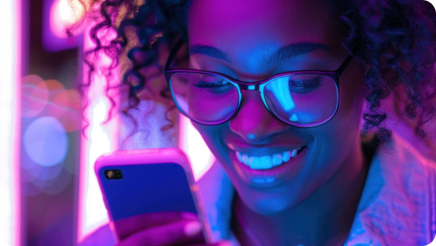Smiling woman with glasses looking at her smartphone under purple and blue neon lights.