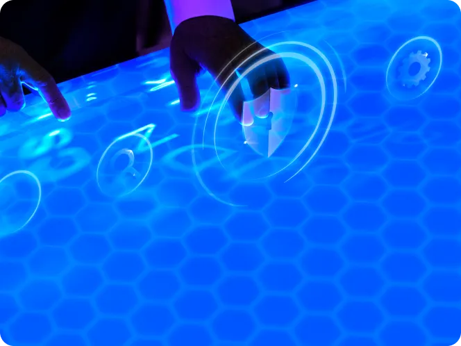 Hands interacting with a bright blue hexagonal touchscreen displaying futuristic icons including a rocket and gear.
