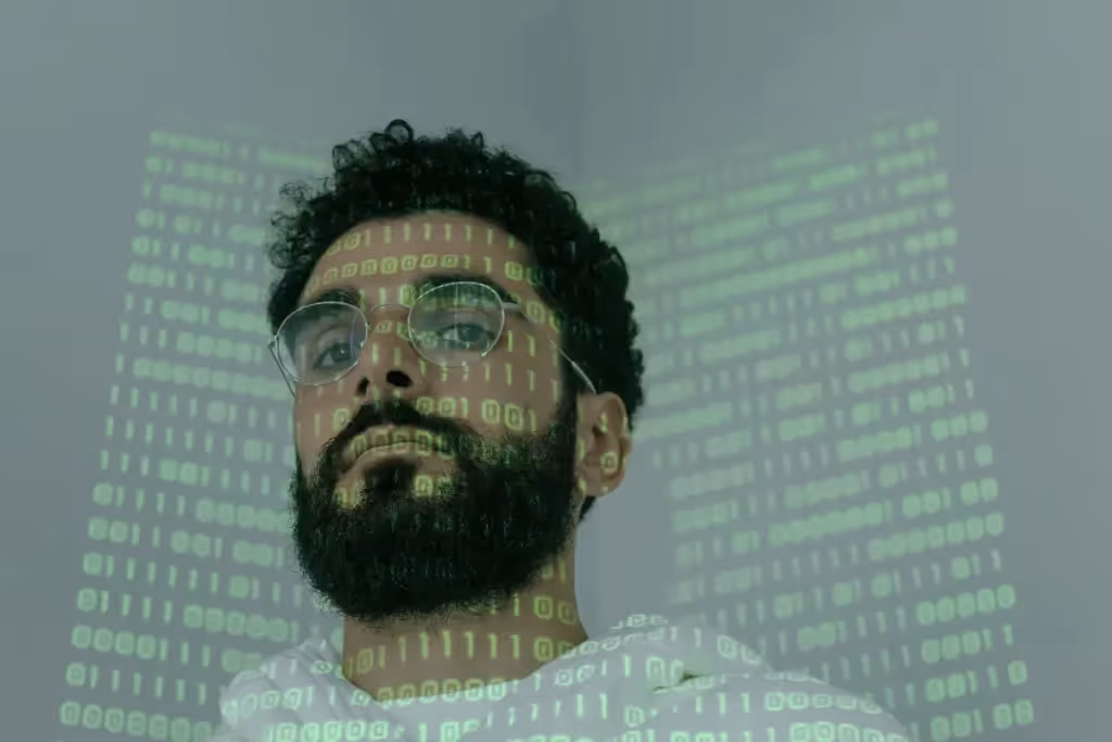Man with glasses and beard, green binary code projected on his face, looking up.