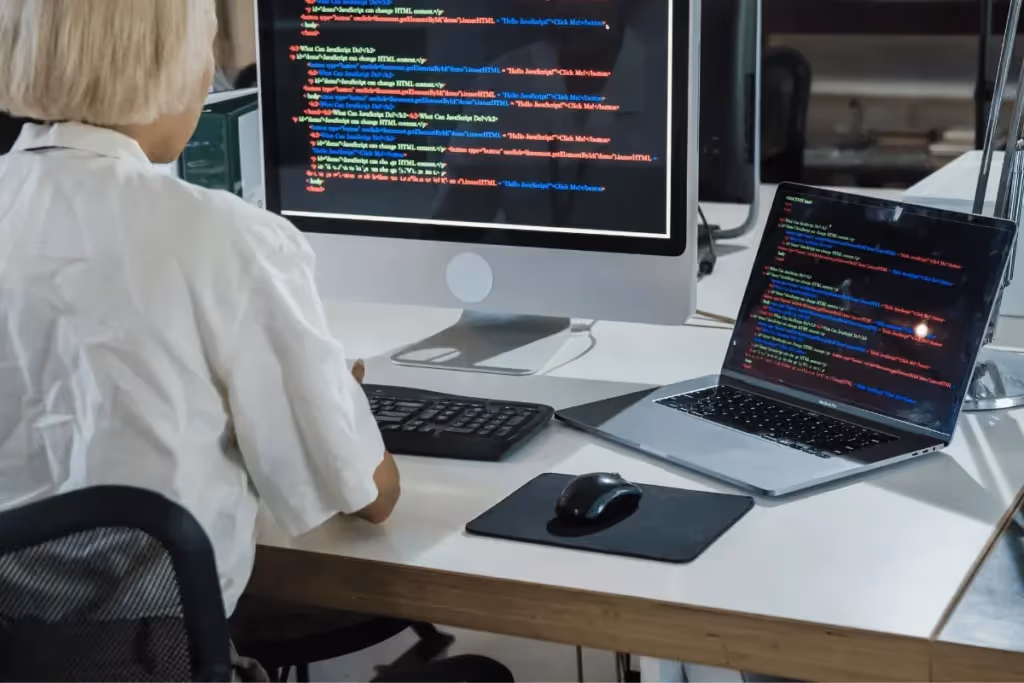A developer working on code displayed on a desktop monitor and a laptop screen in a modern office setup.
