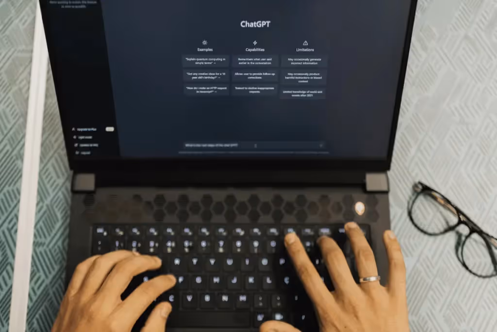 Hands typing on a laptop with ChatGPT interface on screen, showing examples, capabilities, and limitations in a user-friendly design.