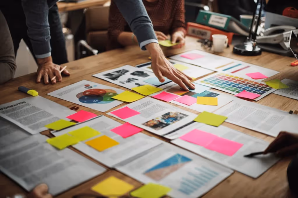 Team collaborating on a project with documents and colorful sticky notes spread across a wooden table.