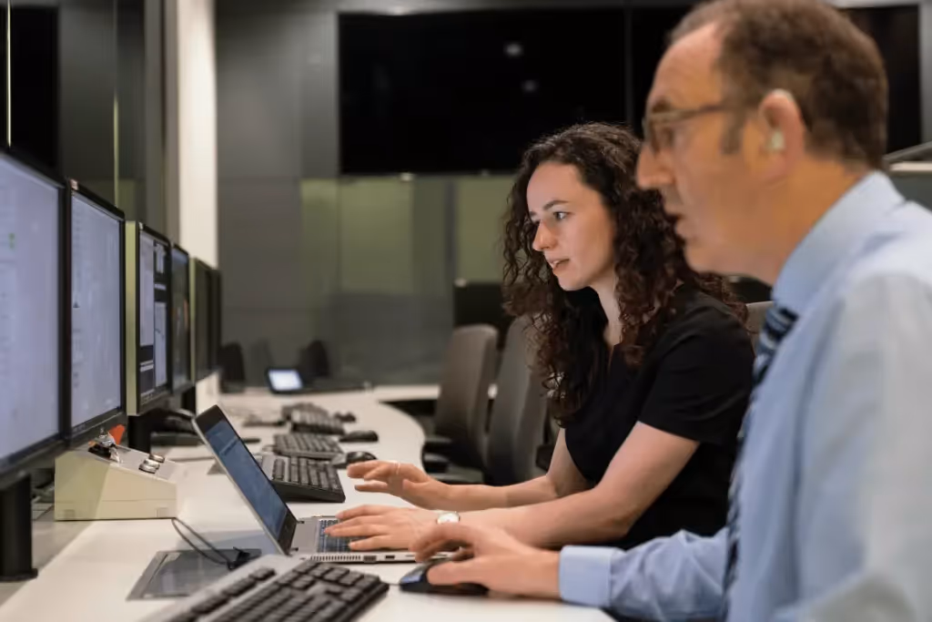 Two professionals working on computers in a modern control room.