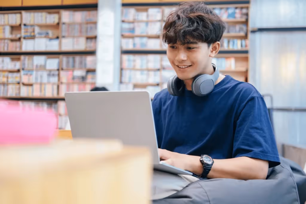 Young man with headphones using a laptop in a library.