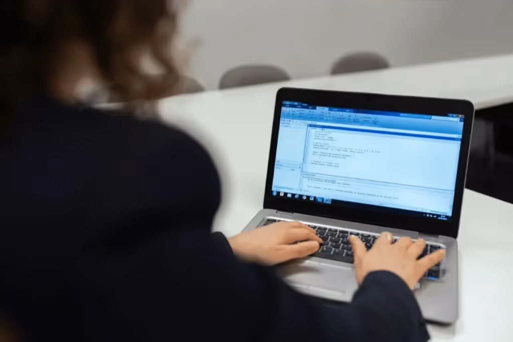 Person coding on a laptop in a well-lit room, writing a program.