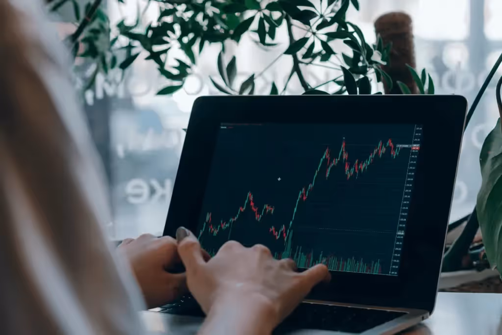 Stock market analysis on a laptop screen with a rising graph and plants in the background.