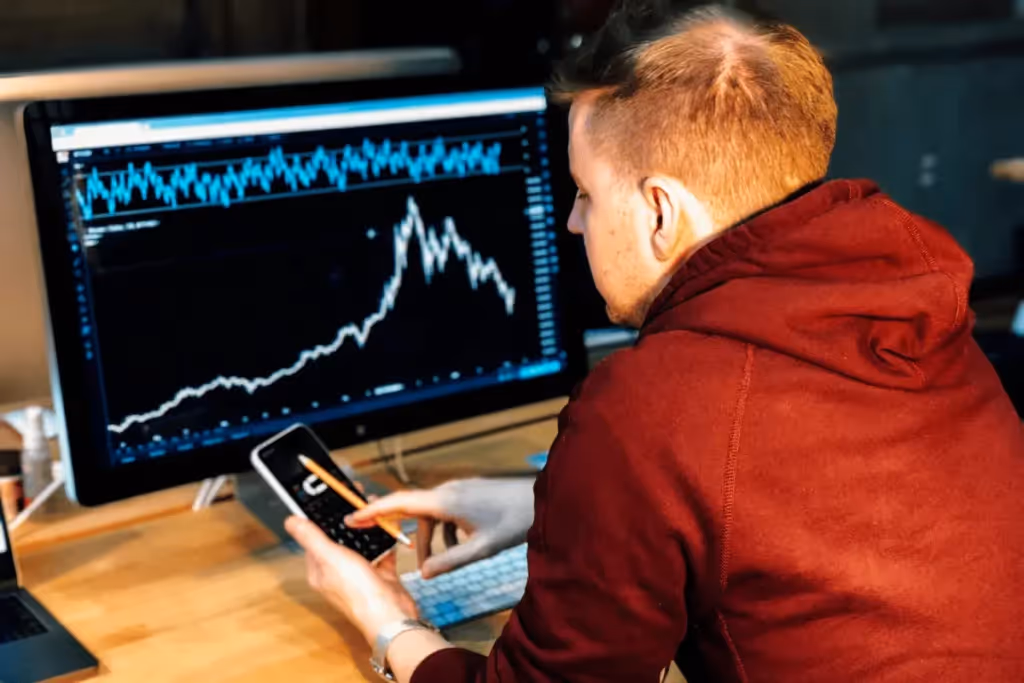 Man analyzing stock market charts on a computer screen, using a calculator.