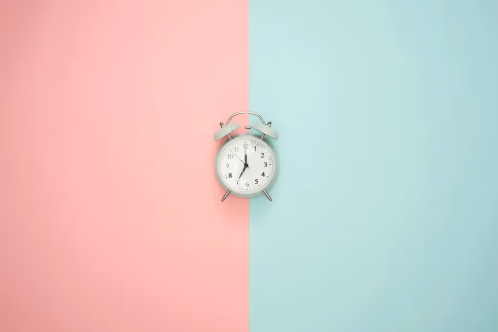 An analog alarm clock centered on a split pink and blue background.