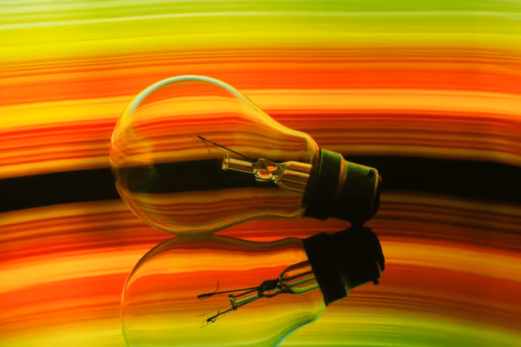 Artistic representation of a light bulb reflecting on a black surface with vivid abstract colors.