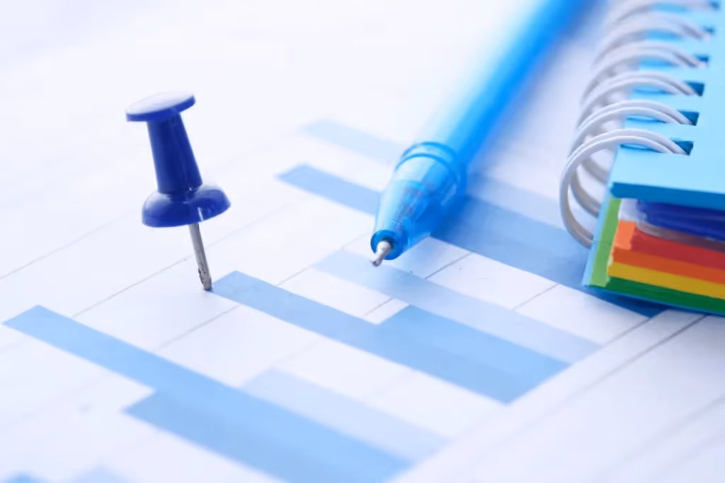 A blue pushpin and pen on a bar graph with a spiral notebook.